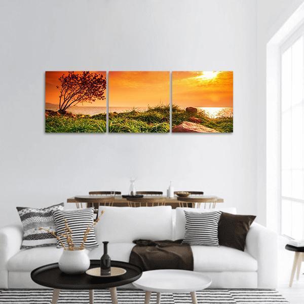 Lone Tree at Lakeside Sunset Panoramic Canvas Wall Art in orange, yellow and green, hung on a wall