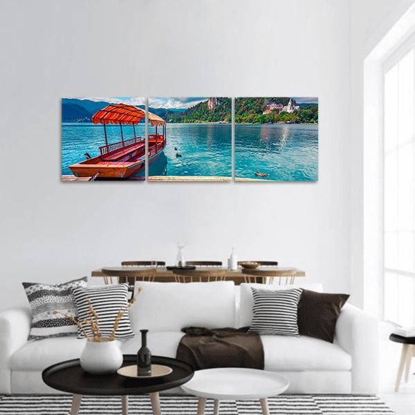 Pletna Boat on Lake Bled Panoramic Canvas Wall Art in orange, green and blue, hung on a wall