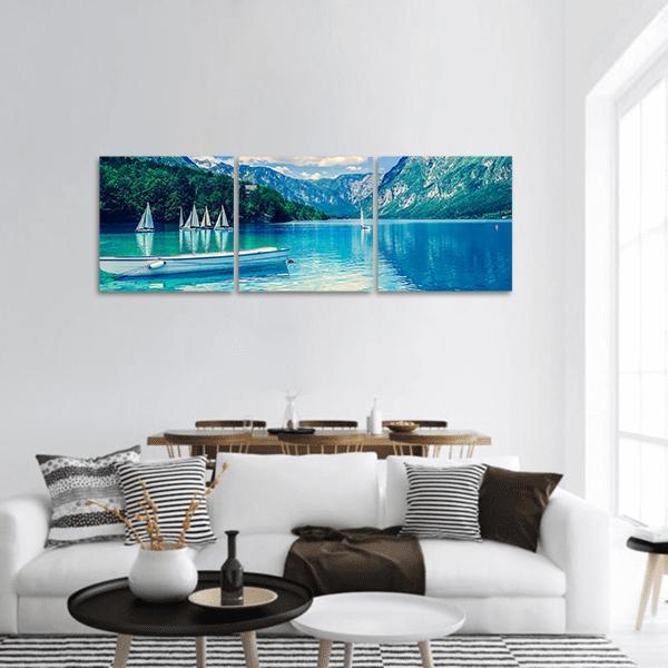 Alpine Lake with White Rowboat and Sailboats Panoramic Canvas Wall Art in white, green and blue, hung on a wall