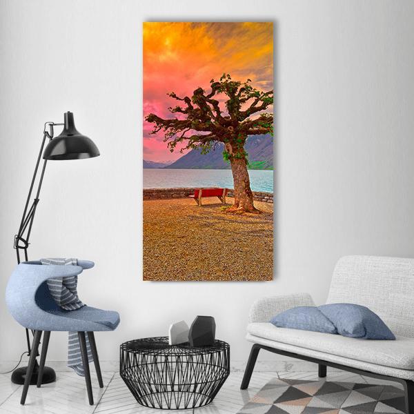 Sunset Lakeside with Knotted Tree and Bench Vertical Canvas Wall Art in brown, orange and pink, single vertical panel hung on a wall