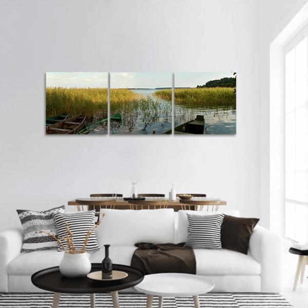 Old Rowboats Among Golden Reeds Panoramic Canvas Wall Art in gold, green and blue, hung on a wall