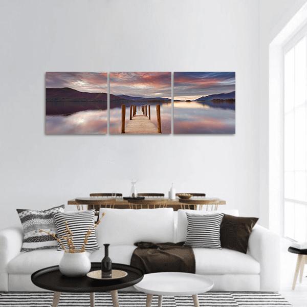 Wooden Jetty Over Calm Lake Panoramic Canvas Wall Art in blue, purple and pink, hung on a wall