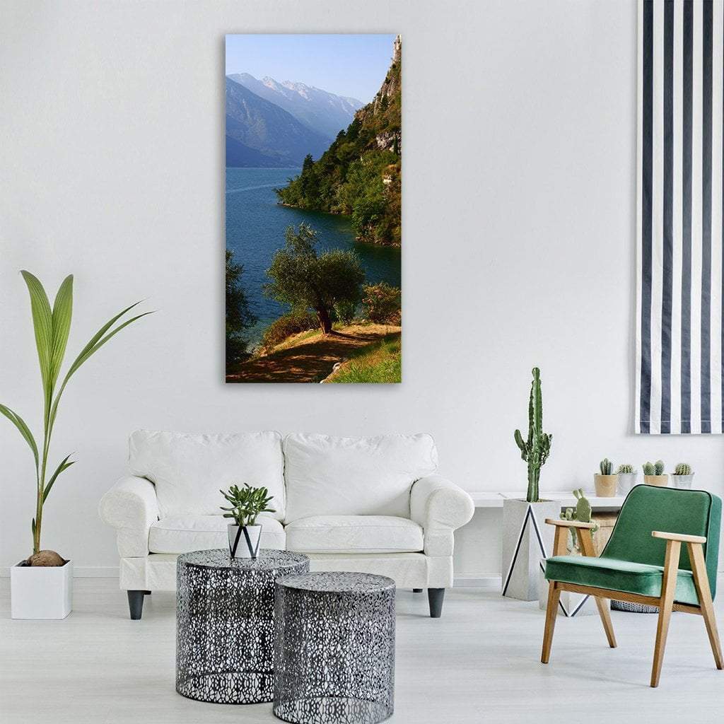 Lakeside Path Beneath Snow-capped Peaks Vertical Canvas Wall Art in gray, green and blue, single vertical panel hung on a wall