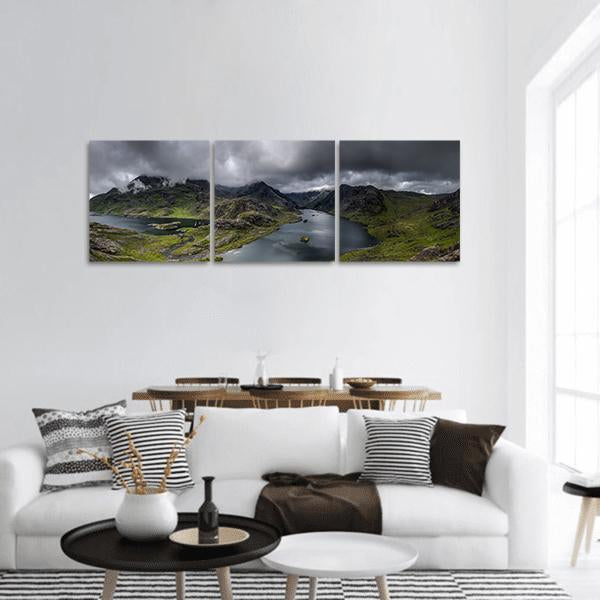 Rugged Mountains Over Reflective Lake Panoramic Canvas Wall Art in gray, green and blue, hung on a wall