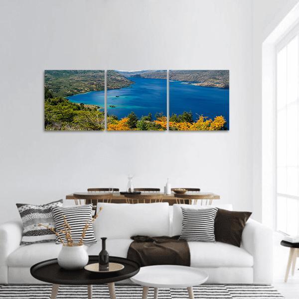 Autumn Lake with Turquoise Bays and Rugged Peaks Panoramic Canvas Wall Art in orange, green and blue, hung on a wall