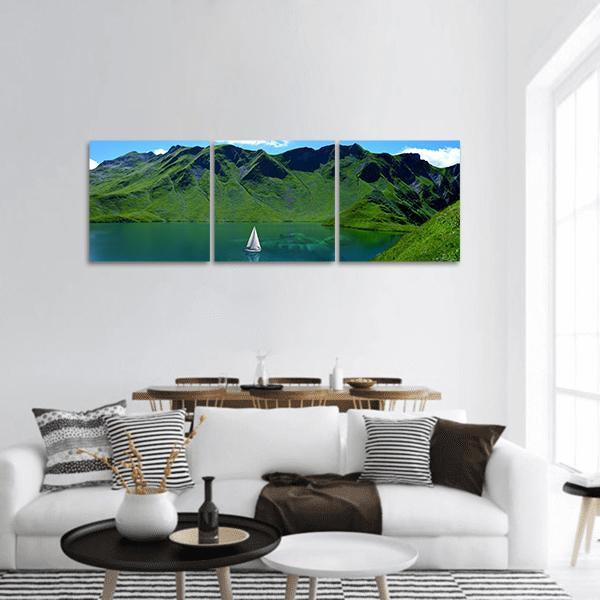 Alpine Lake with White Sailboat Panoramic Canvas Wall Art in green and blue, hung on a wall