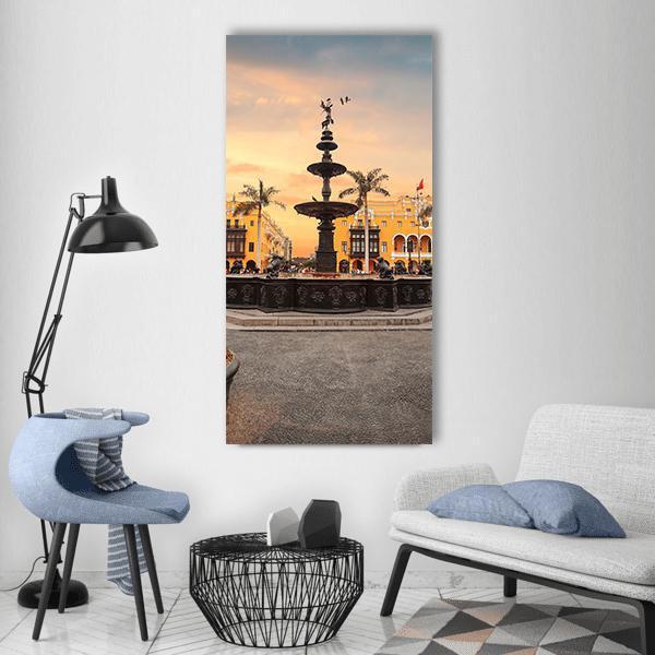 Lima Main Square Fountain at Dusk Vertical Canvas Wall Art in gray, orange and yellow, single vertical panel hung on a wall