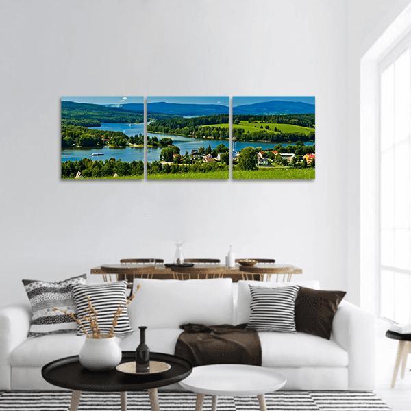 Lakeside Village by Blue Lake Panoramic Canvas Wall Art in green and blue, hung on a wall
