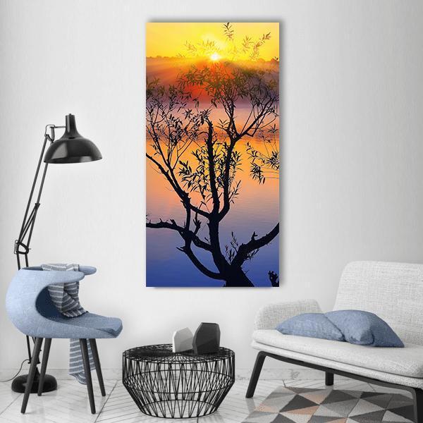 Tree Silhouette at Sunrise Vertical Canvas Wall Art in orange, yellow and blue, single vertical panel hung on a wall