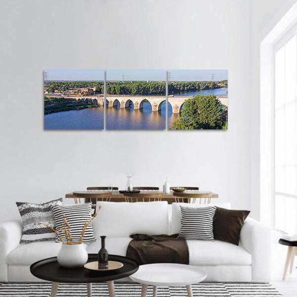 Multi-arched Stone Bridge Over Blue River Panoramic Canvas Wall Art in beige, green and blue, hung on a wall