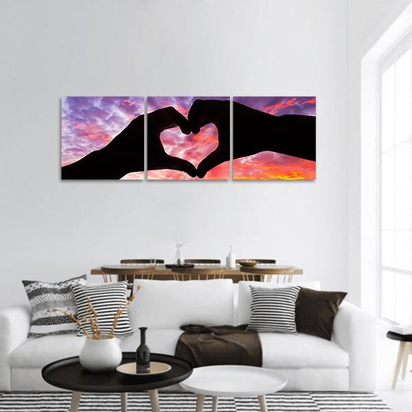Hands Forming Heart Silhouette Panoramic Canvas Wall Art in black, orange and purple, hung on a wall