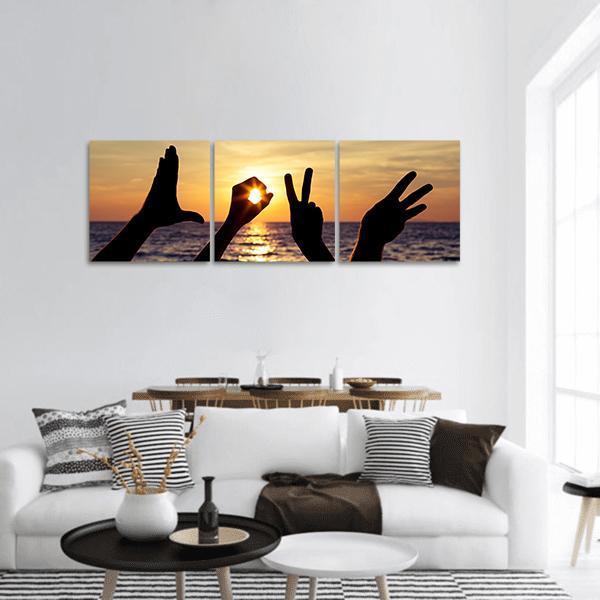 Hand Silhouettes Spelling Love at Sunset Panoramic Canvas Wall Art in black, orange and yellow, hung on a wall