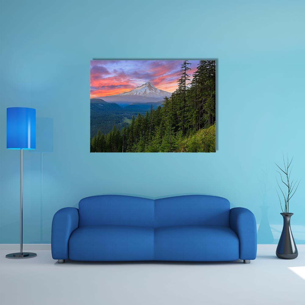 Snow-capped Mountain Sunset Over Evergreen Forest Canvas Wall Art in orange, green and pink, single panel hung on a wall