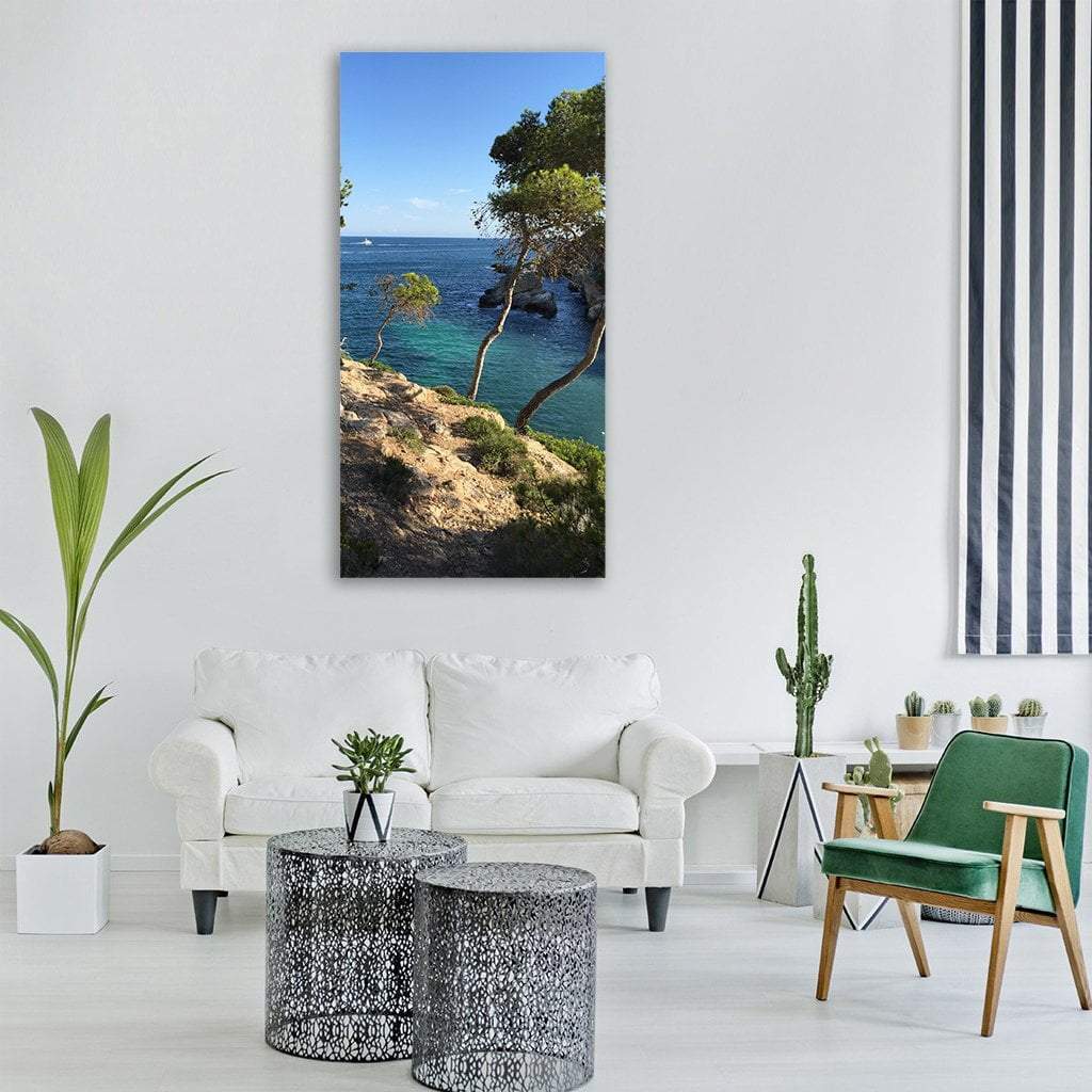 Mallorca Cliffs with Pine Trees and Turquoise Sea Vertical Canvas Wall Art in brown, green and blue, single vertical panel hung on a wall