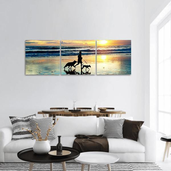 Person Running with Dogs on Beach at Sunset Panoramic Canvas Wall Art in orange, yellow and blue, hung on a wall