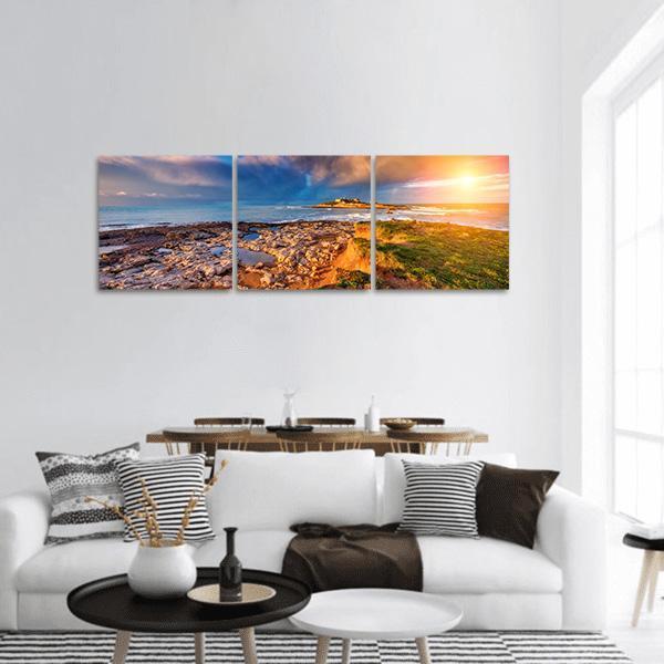 Sunset Over Rocky Coastline Panoramic Canvas Wall Art in orange, yellow and blue, hung on a wall