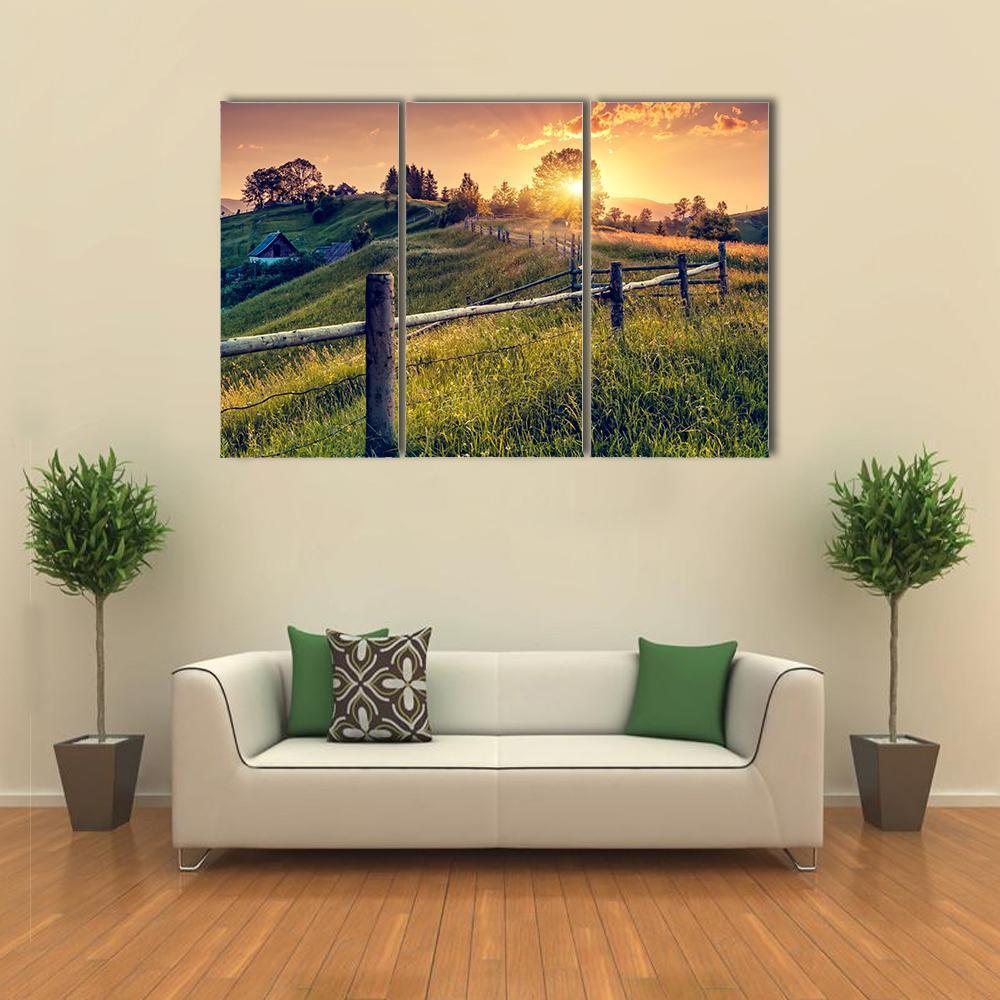 Sunset Farmhouse with Wooden Fence Canvas Wall Art in orange, yellow and green, 3 panel horizontal set hung on a wall