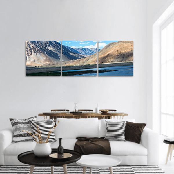 Blue Lake Beneath Sharp Mountain Ridges Panoramic Canvas Wall Art in gray, brown and blue, hung on a wall