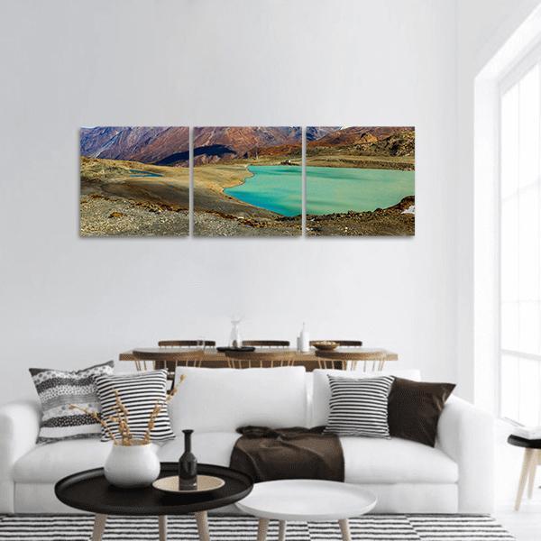 Turquoise Lake in the Alps Panoramic Canvas Wall Art in brown, green and blue, hung on a wall