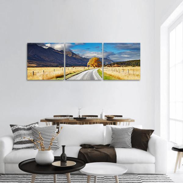 Mountain Road Under Clouds Panoramic Canvas Wall Art in gray, yellow and blue, hung on a wall