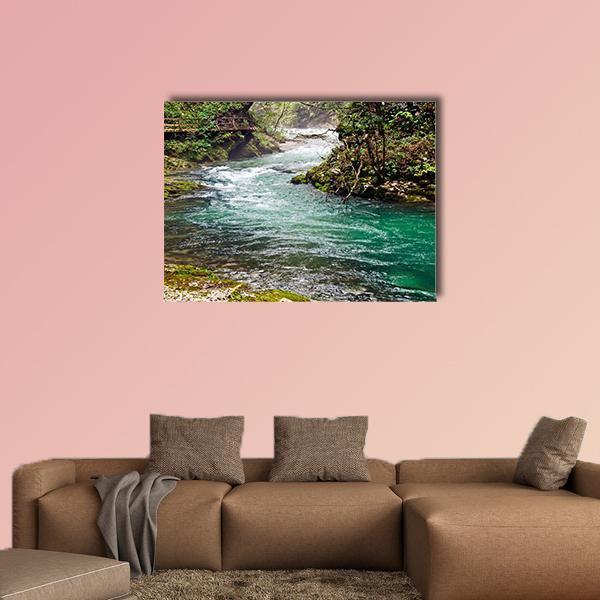 Turquoise Mountain River with Wooden Bridge Canvas Wall Art in brown, green and blue, single panel hung on a wall