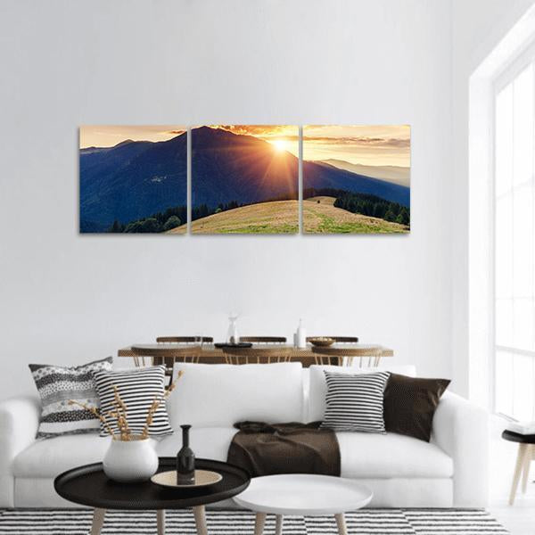 Sunbeams Over Mountain Ridge and Meadow Panoramic Canvas Wall Art in yellow, green and blue, hung on a wall