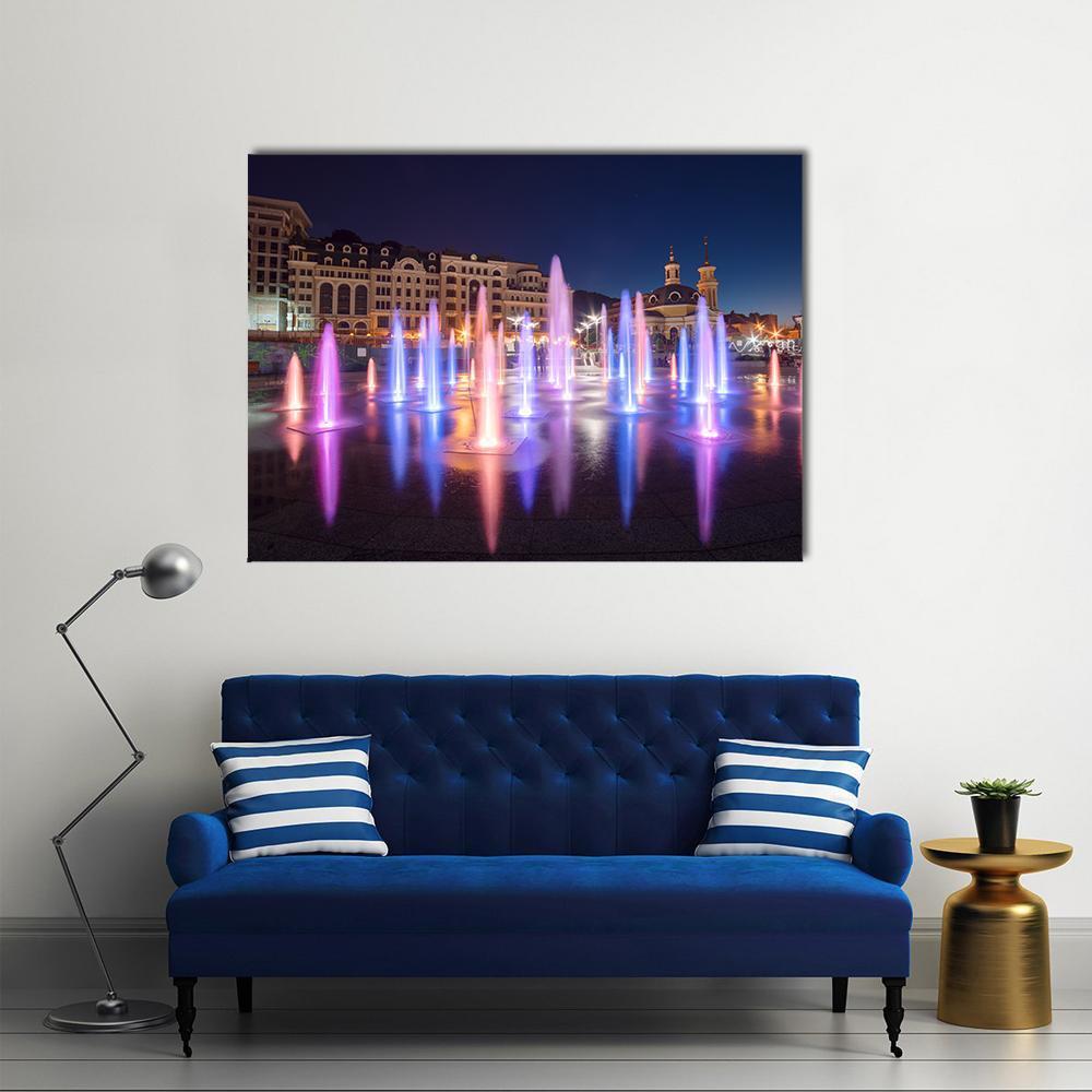 Vibrant Night Cityscape with Colorful Fountains Canvas Wall Art in blue, purple and pink, single panel hung on a wall