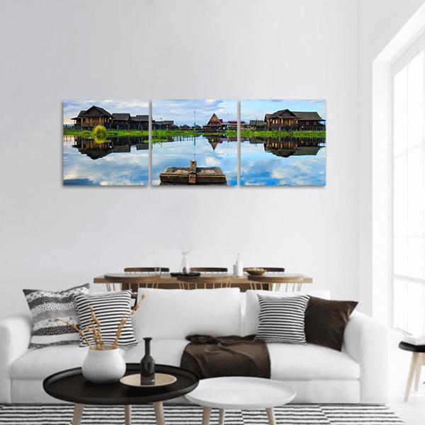Boat Among Stilt Houses and Reflections Panoramic Canvas Wall Art in brown, green and blue, hung on a wall
