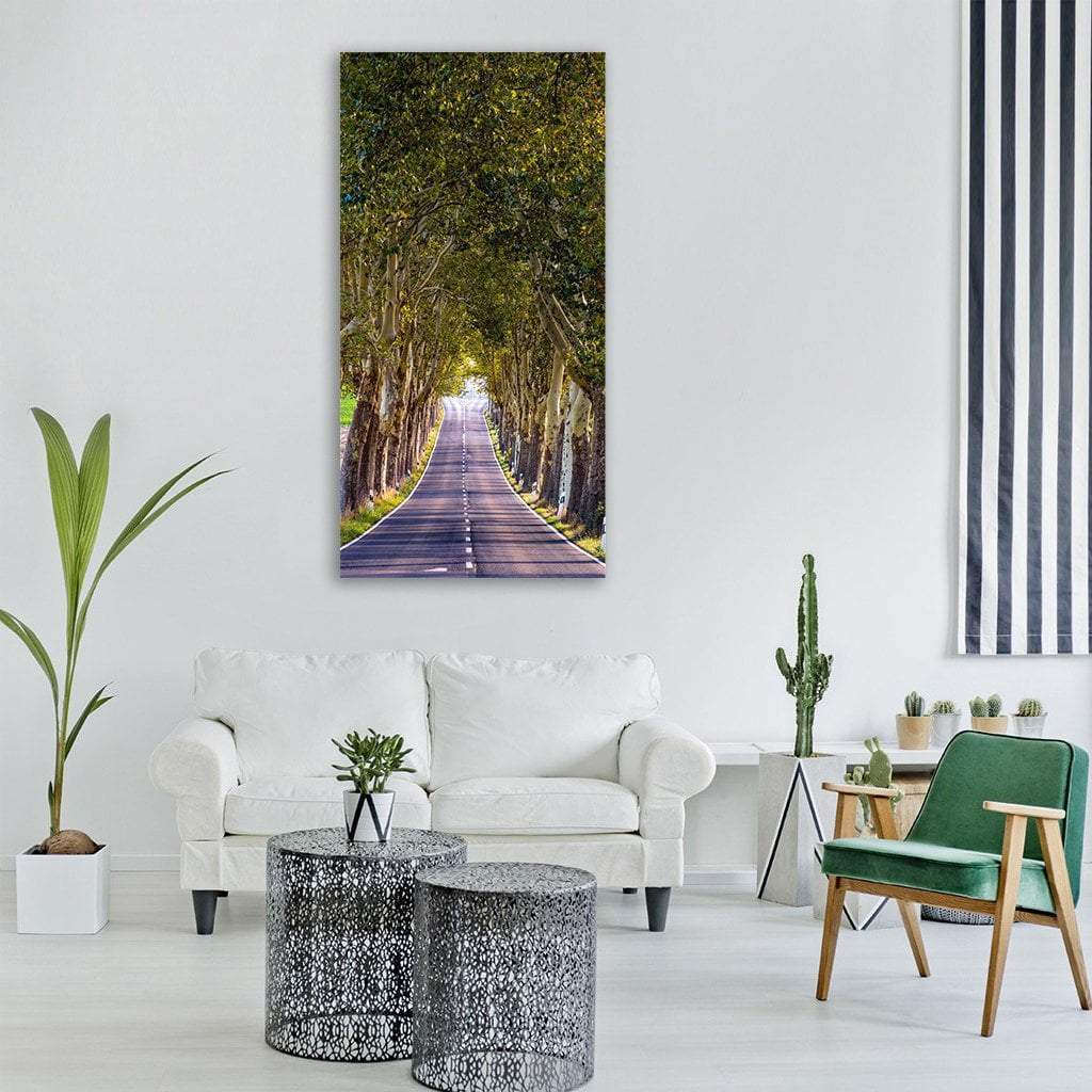Tree-lined Road with Dappled Sunlight Vertical Canvas Wall Art in brown, yellow and green, single vertical panel hung on a wall