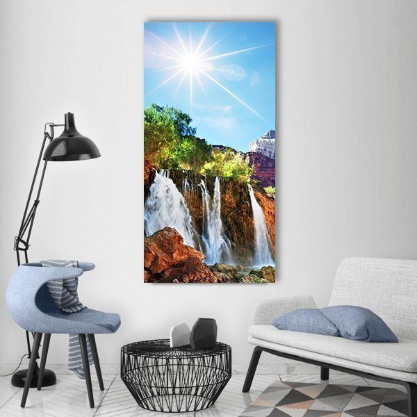Sunlit Waterfall with Reddish-brown Rocks Vertical Canvas Wall Art in white, brown and blue, single vertical panel hung on a wall