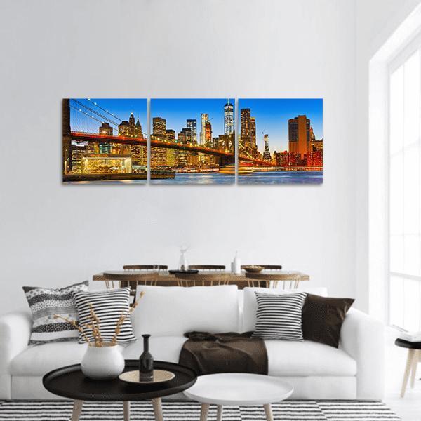 Manhattan Skyline with Brooklyn Bridge at Night Panoramic Canvas Wall Art in black, orange and blue, hung on a wall
