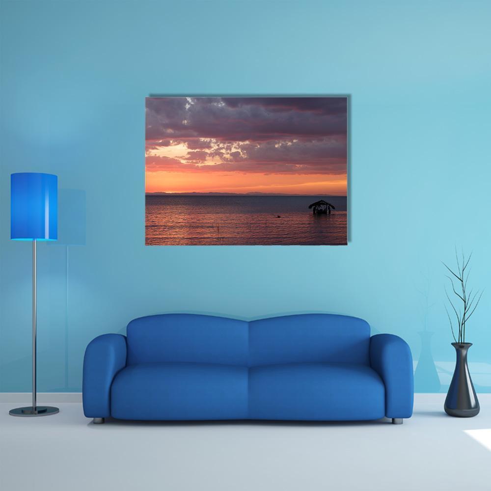Sunset Over Lake with Stilt Hut Canvas Wall Art in orange, blue and purple, single panel hung on a wall