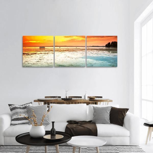 Sunset Over Beach with Silhouetted Boat Panoramic Canvas Wall Art in orange, yellow and blue, hung on a wall