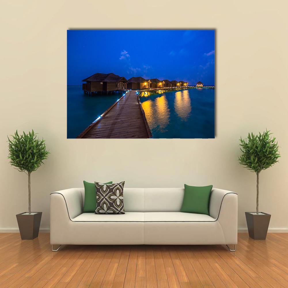 Illuminated Overwater Bungalows at Night Canvas Wall Art in yellow, blue and navy, single panel hung on a wall