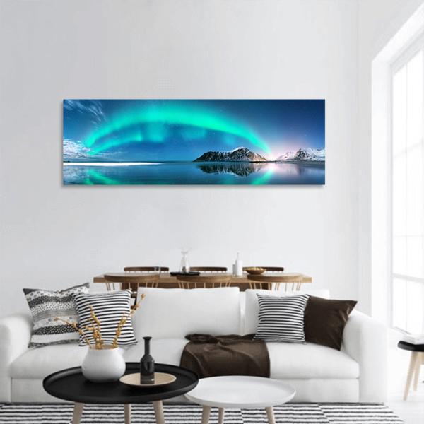 Turquoise Aurora Over Snow-capped Mountains Panoramic Canvas Wall Art in white, green and blue, hung on a wall
