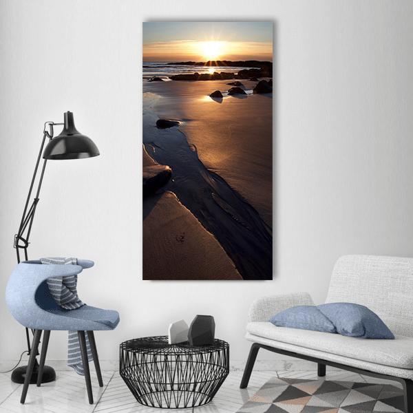 Ocean Rocks and Beach at Dawn with Sun Flares Vertical Canvas Wall Art in brown, orange and yellow, single vertical panel hung on a wall