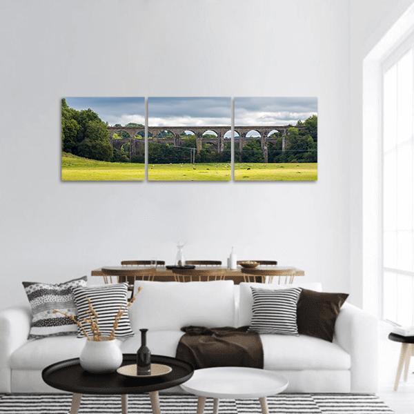 Stone Aqueduct and Viaduct Over Green Meadow Panoramic Canvas Wall Art in gray, green and blue, hung on a wall