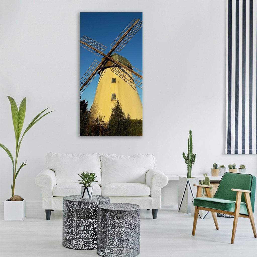 Sunlit Old Windmill with Wooden Lattice Sails Vertical Canvas Wall Art in brown, yellow and blue, single vertical panel hung on a wall