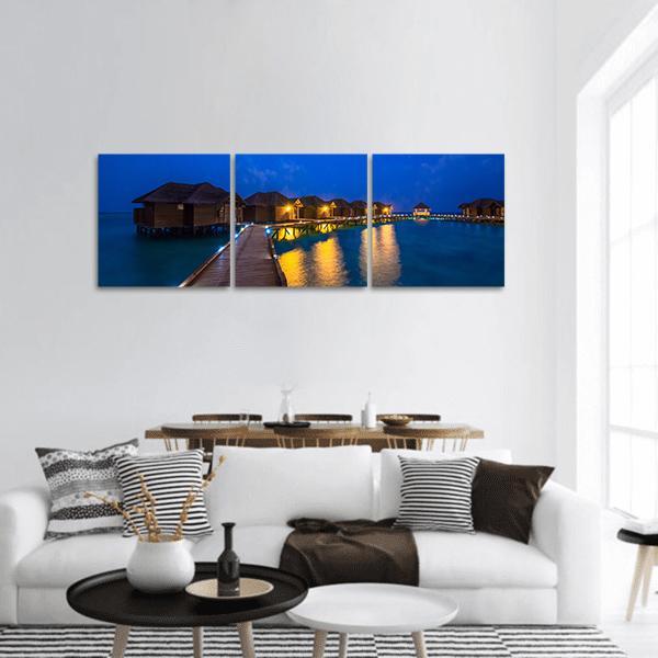 Overwater Bungalows at Night Panoramic Canvas Wall Art in brown, yellow and blue, hung on a wall