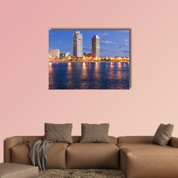 Evening Waterfront Cityscape with Glowing Reflections Canvas Wall Art in orange, yellow and blue, single panel hung on a wall