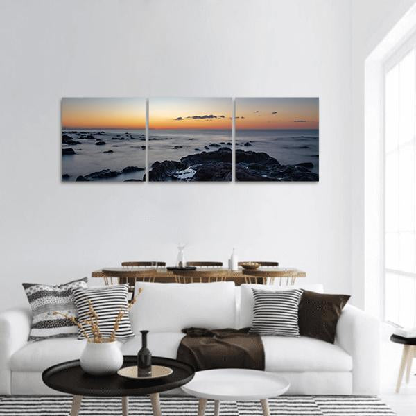 Sunrise at Palmasera Beach Panoramic Canvas Wall Art in black, orange and blue, hung on a wall