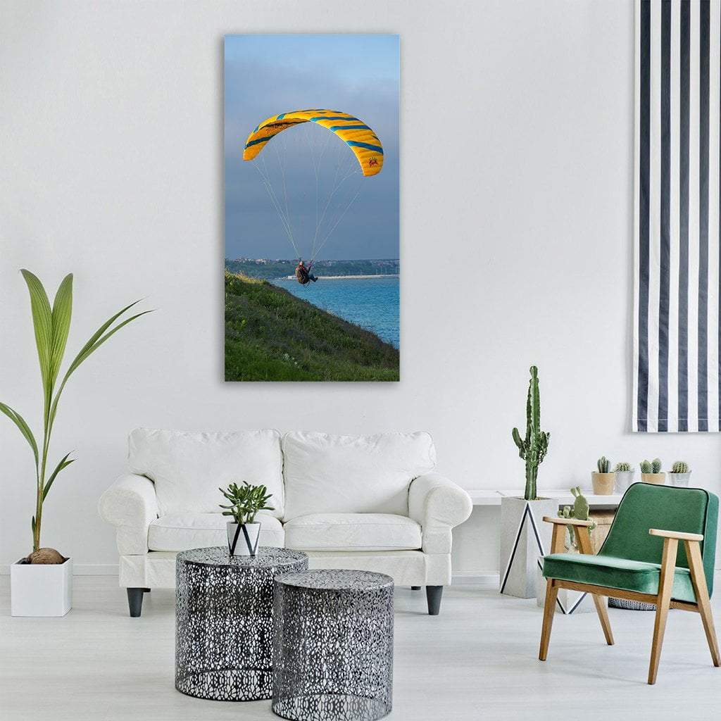 Paraglider Over Coastal Cliff Vertical Canvas Wall Art in yellow, green and blue, single vertical panel hung on a wall