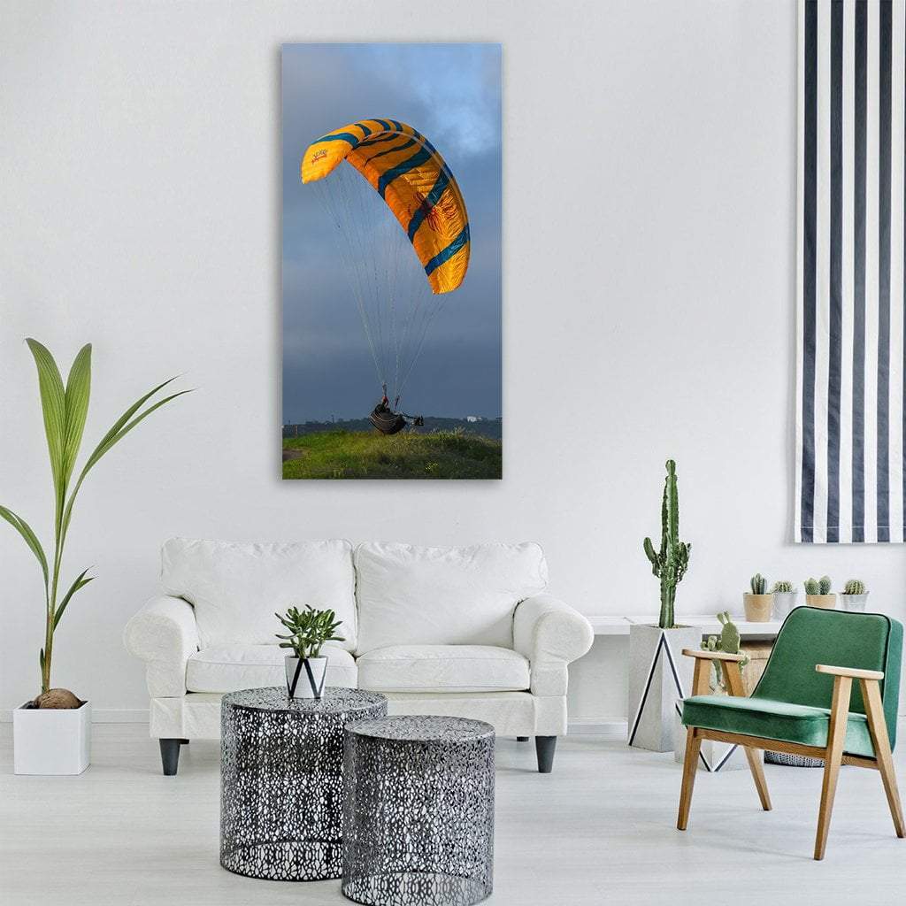 Orange and Blue Paraglider Over Hill Vertical Canvas Wall Art in gray, orange and blue, single vertical panel hung on a wall