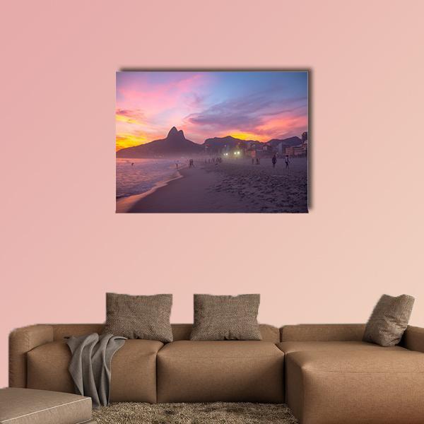 People Walking on Beach at Sunset Canvas Wall Art in orange, purple and pink, single panel hung on a wall