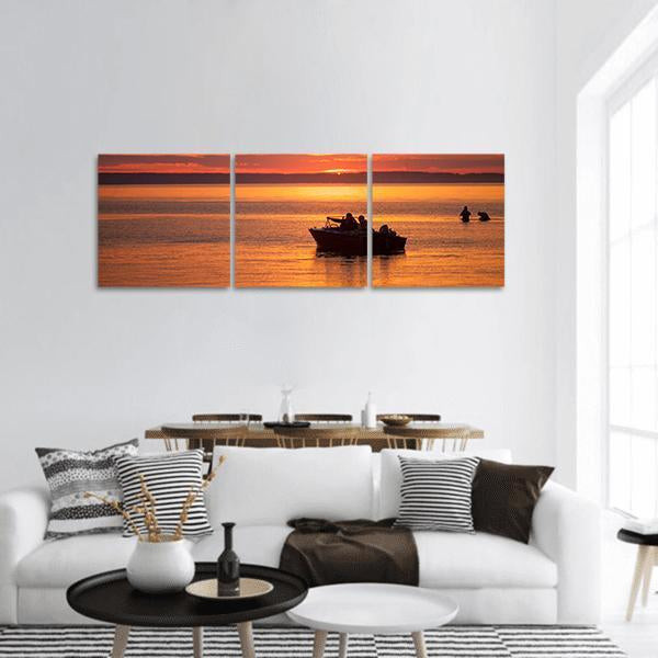 People Sailing at Sunset Panoramic Canvas Wall Art in black, orange and yellow, hung on a wall