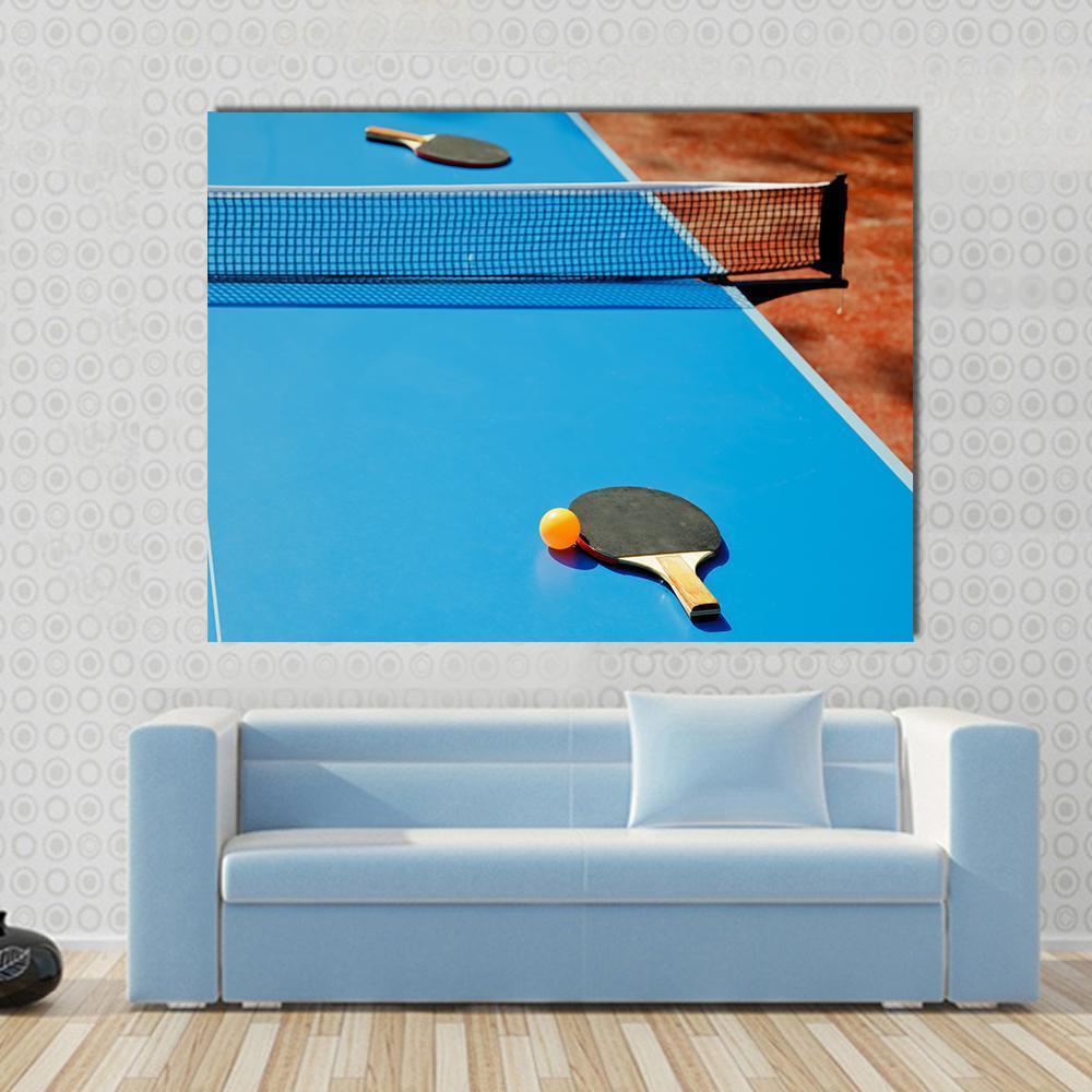 Ping Pong Ball with Paddle on Tennis Table Canvas Wall Art in black, orange and blue, single panel hung on a wall