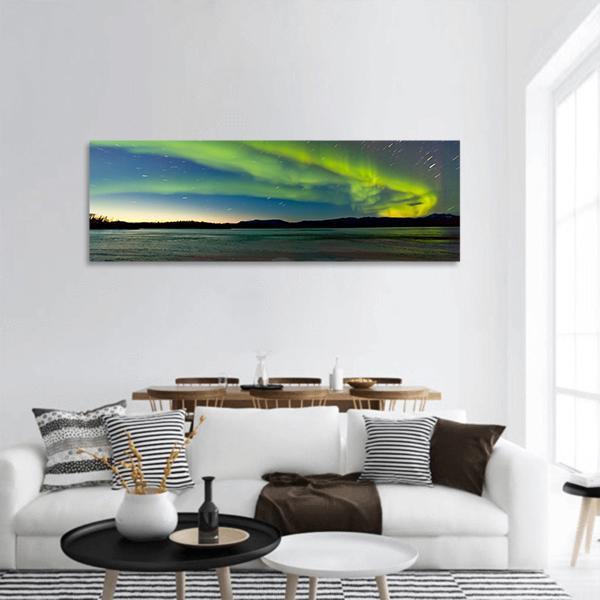 Aurora Borealis Over Canadian Mountains and Water Panoramic Canvas Wall Art in yellow, green and blue, hung on a wall