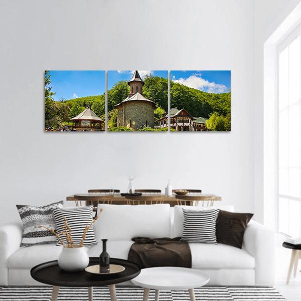 Prislop Monastery Among Green Hills Panoramic Canvas Wall Art in brown, green and blue, hung on a wall