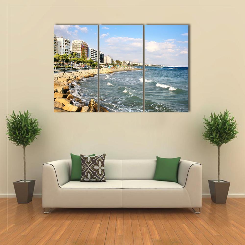 Sunny Rocky Beach with Coastal Buildings Canvas Wall Art in white, beige and blue, 3 panel horizontal set hung on a wall