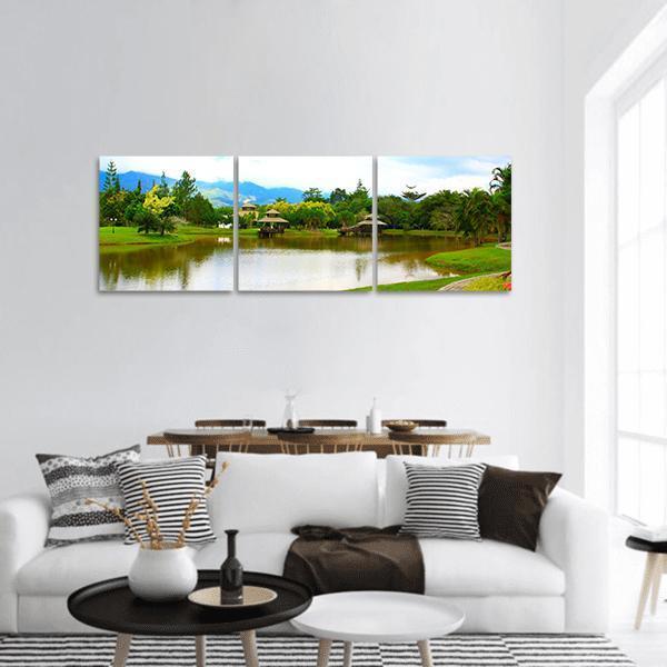 Wooden Pavilions Over Serene Lake Panoramic Canvas Wall Art in brown, green and blue, hung on a wall